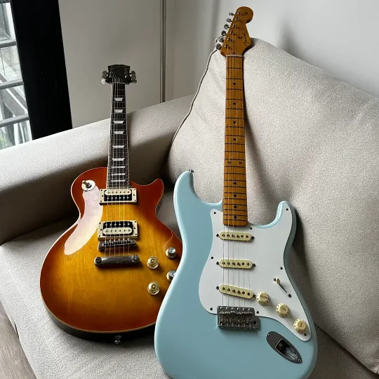 A sunburst Les Paul and a pale blue Stratocaster leaning on a sofa