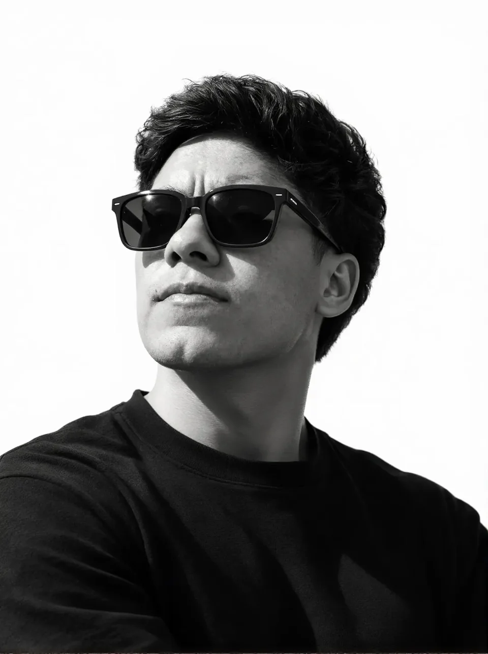 Portrait of Moiséz in black and white: sunglasses, a black sweater, looking up and to the left