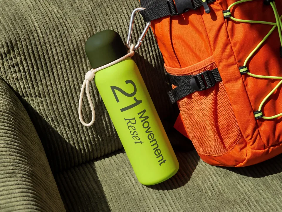 21 Movement Reset: Lime water bottle with the stacked wordmark, next to an orange backpack