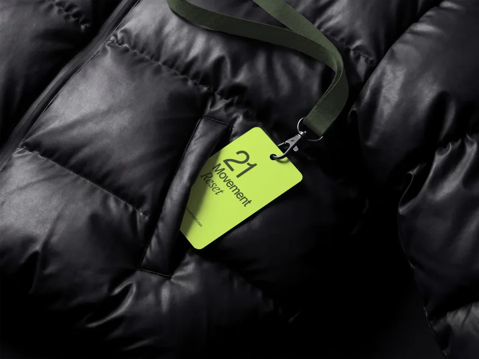 21 Movement Reset: Lime ID card on an olive lanyard, over a black puffer jacket